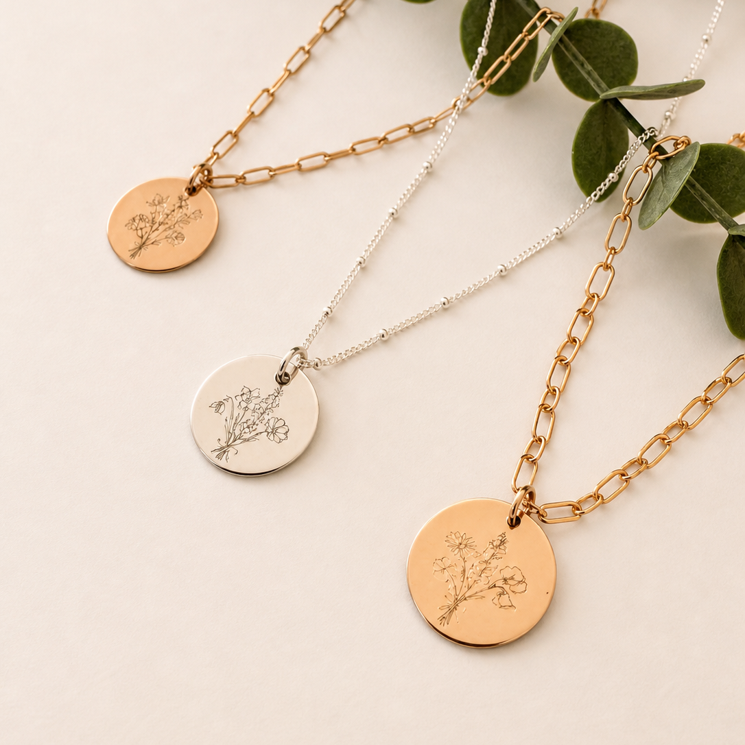 Three botanical engraved necklaces with circular pendants on a light background with green leaves.