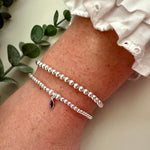 Silver bracelet on a wrist with a white sleeve and green leaves in the background