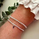 Silver bracelet on a wrist with a white sleeve and green leaves in the background