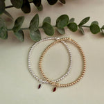 Two beaded bracelets on a light surface with green leaves in the background