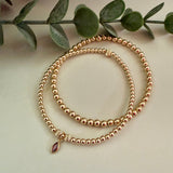 Gold filled beaded bracelet with a birthstone charm on a light background with green leaves.