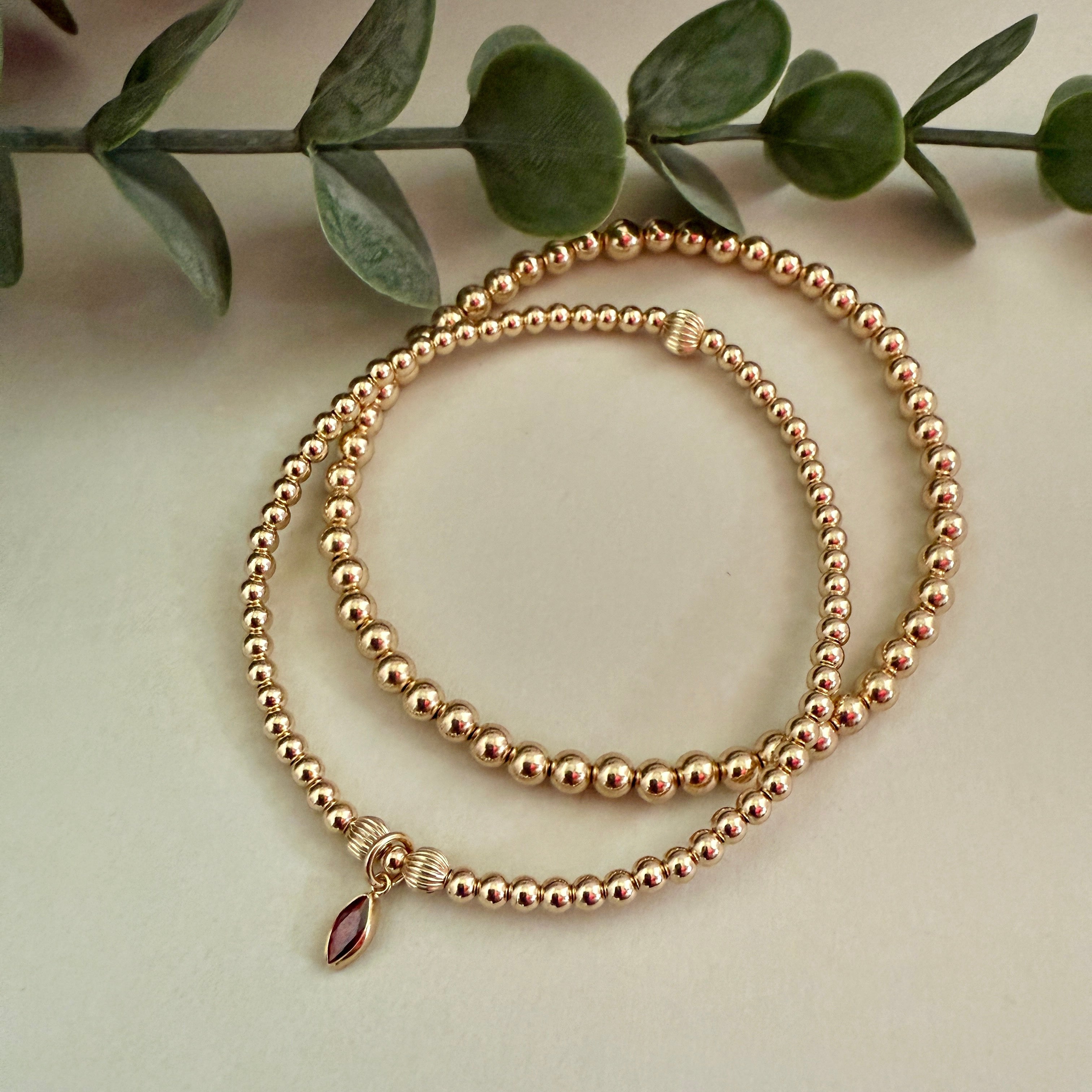 Gold filled beaded bracelet with a birthstone charm on a light background with green leaves.