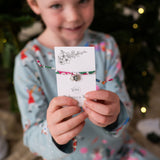 Child holding a liberty bracelet with a card, Christmas tree in the background