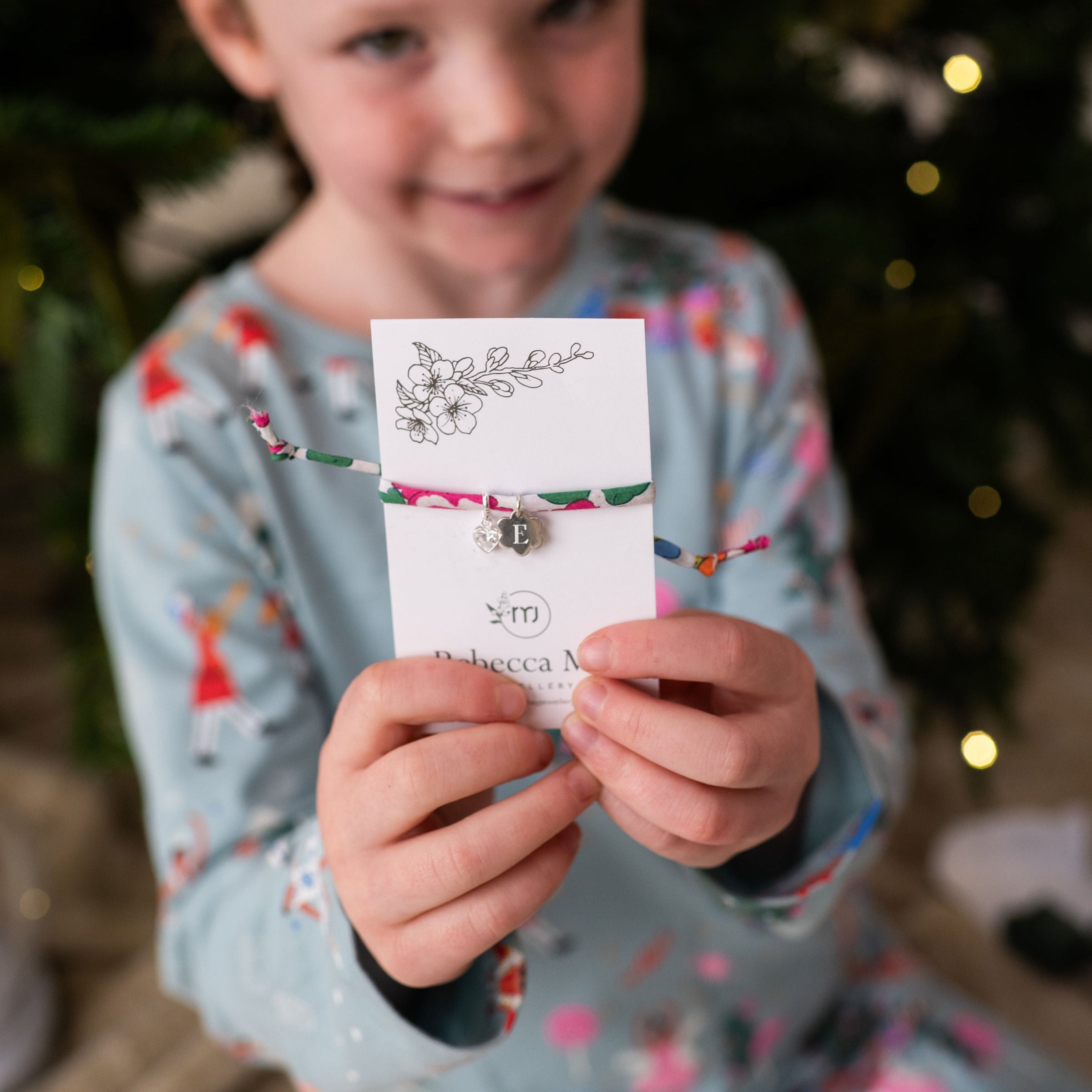 Child holding a liberty bracelet with a card, Christmas tree in the background