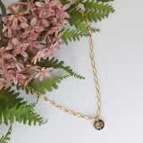 Botanical necklace with birth flower pendant beside dusky pink flowers.