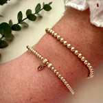 Gold beaded bracelet with a purple gemstone on a wrist, with a light background and green leaves.