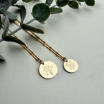 Two gold necklaces with circular pendants on a light gray background with green leaves.