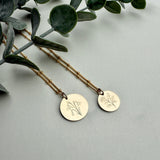 Two gold necklaces with circular pendants on a light gray background with green leaves.
