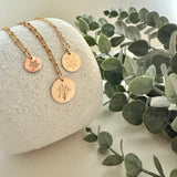 Three gold necklaces with engraved designs on a stone surface with green leaves in the background