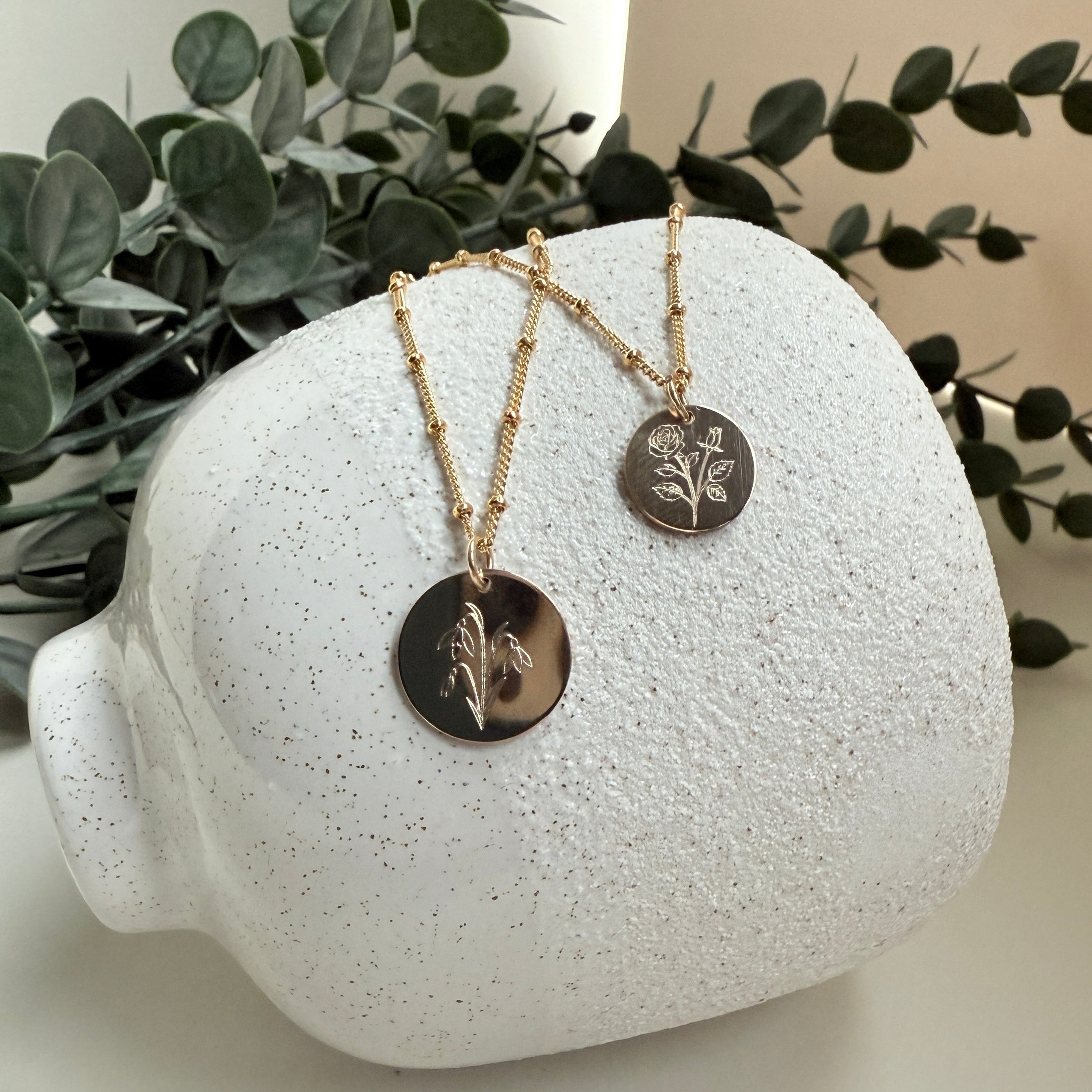 Necklace displayed on a white textured stand with green leaves in the background