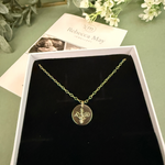 Gold filled family bouquet necklace with a pendant in a box on a green surface with flowers and a card. Flowers on pendant are snowdrop, Larkspur and cosmos
